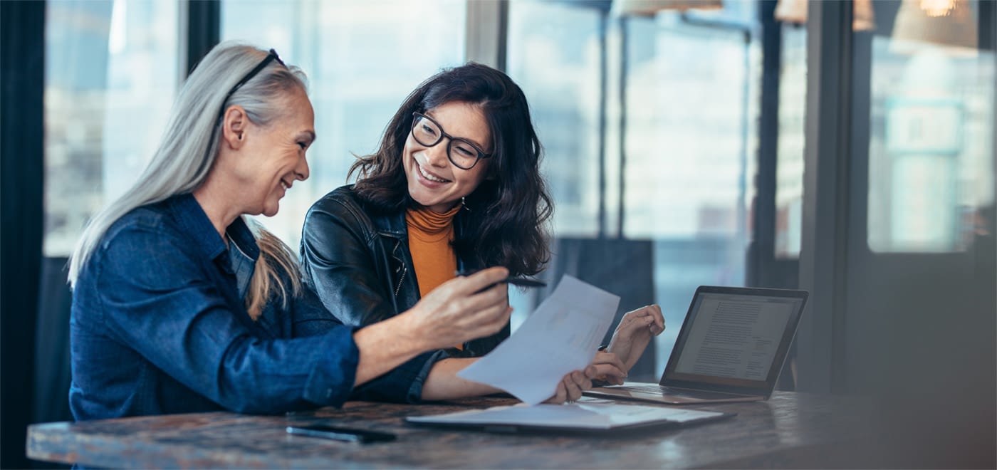 Two women cheerfully reviewing some documentation at a desk.