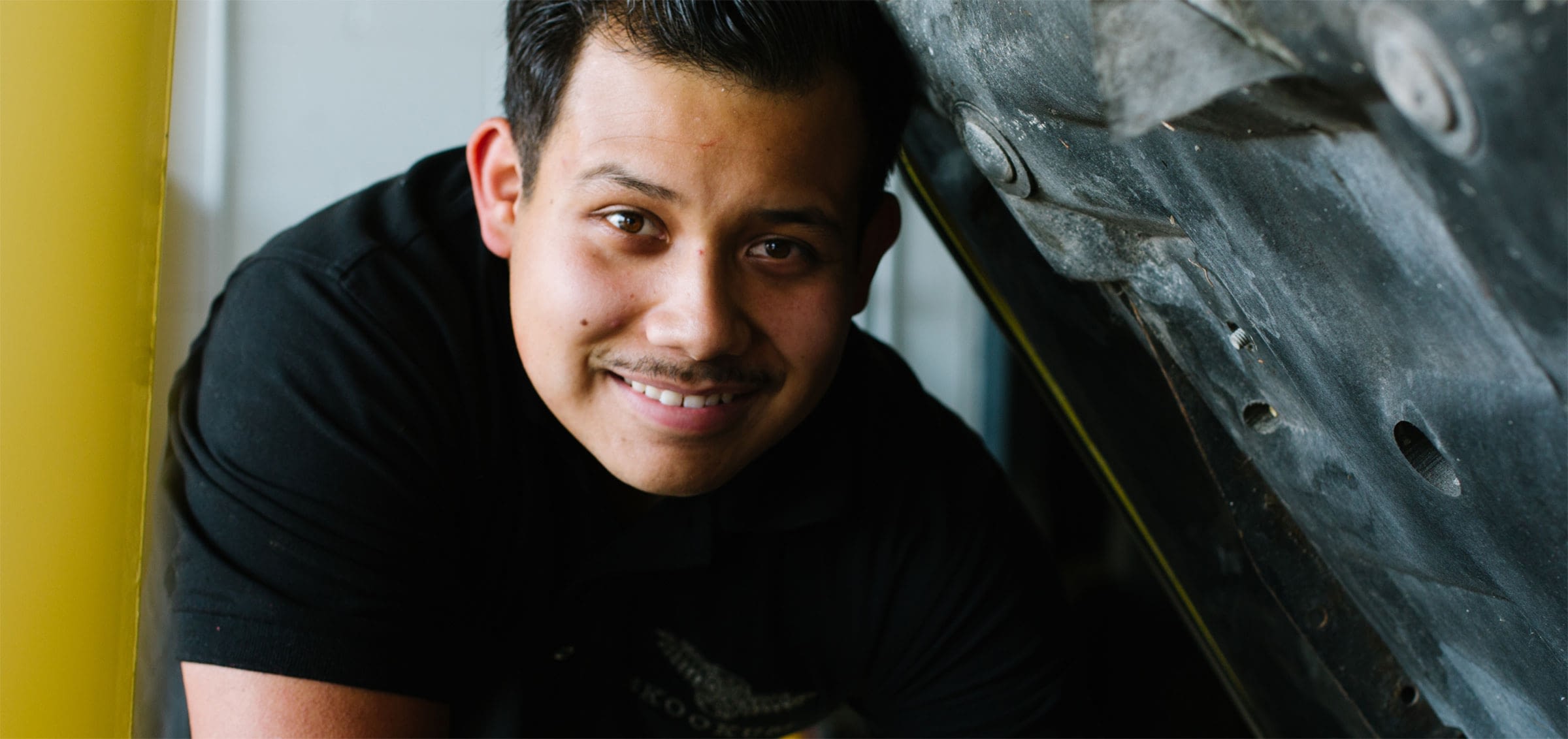 Close-up shot of mechanic smiling and working under a hood.