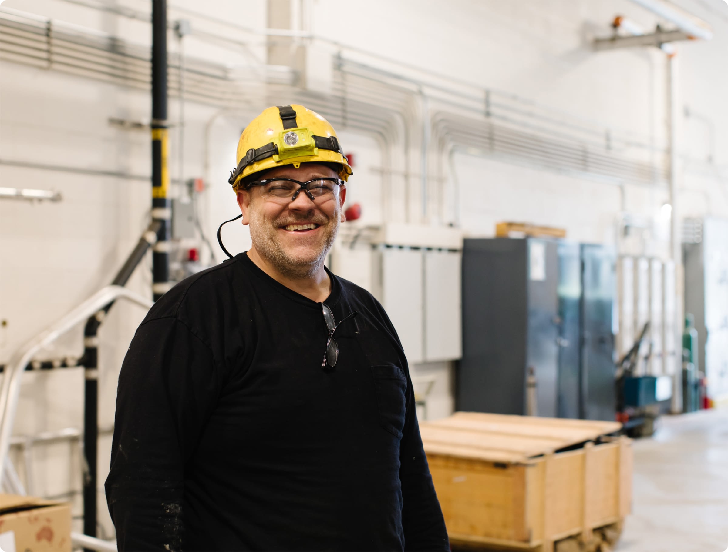 Warehouse employee in yellow hard hat looking happy and safe in large facility.
