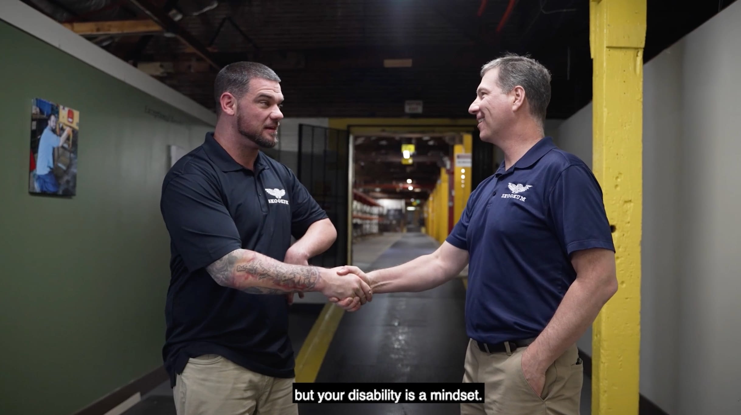 Skookum CEO Jeff Dolven (right) shakes hands with a Skookum employee in an industrial workplace. A subtitle at the bottom reads, “but your disability is a mindset.”