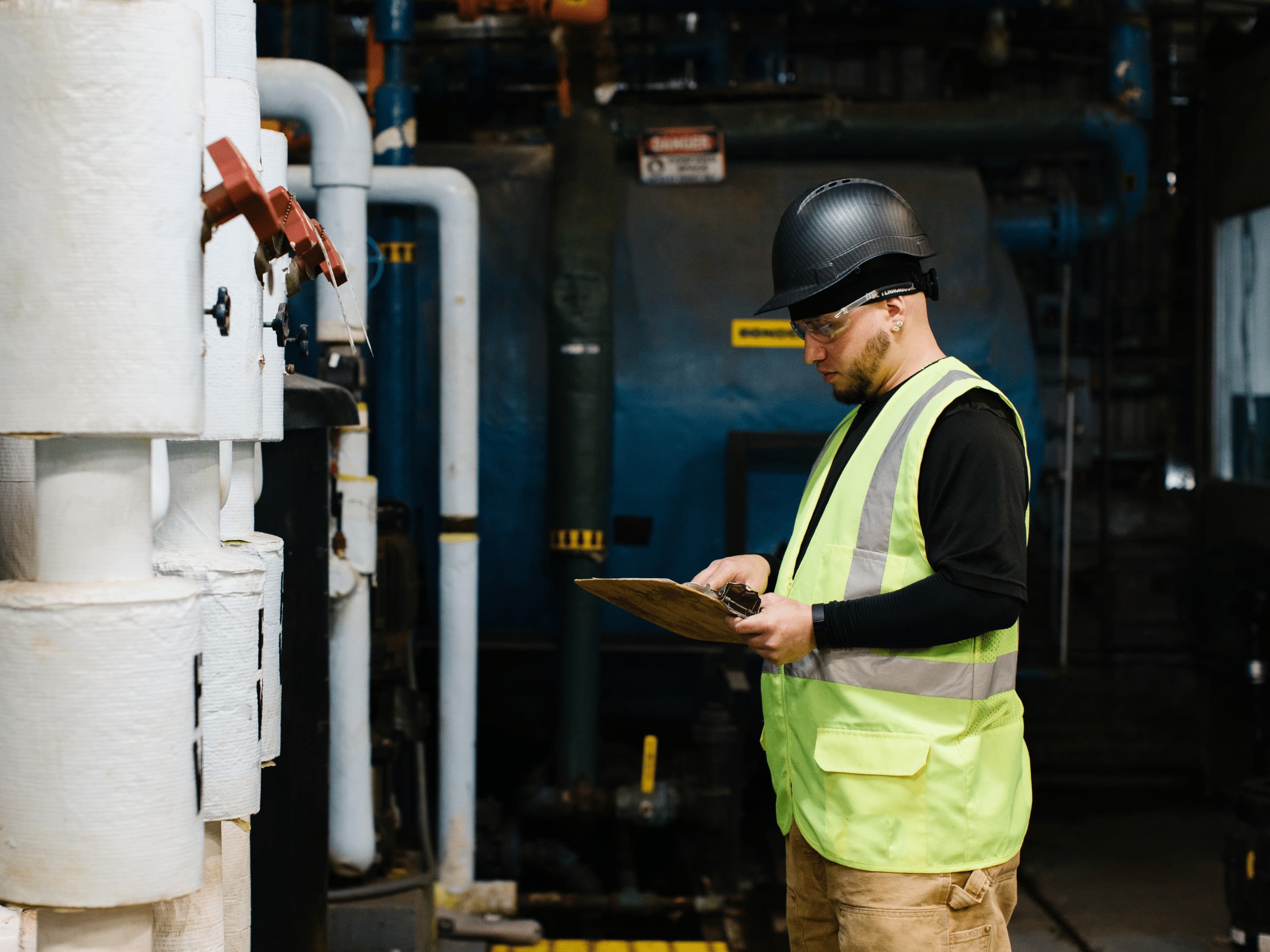 Employee in safety vest and hard hat checking on equipment.