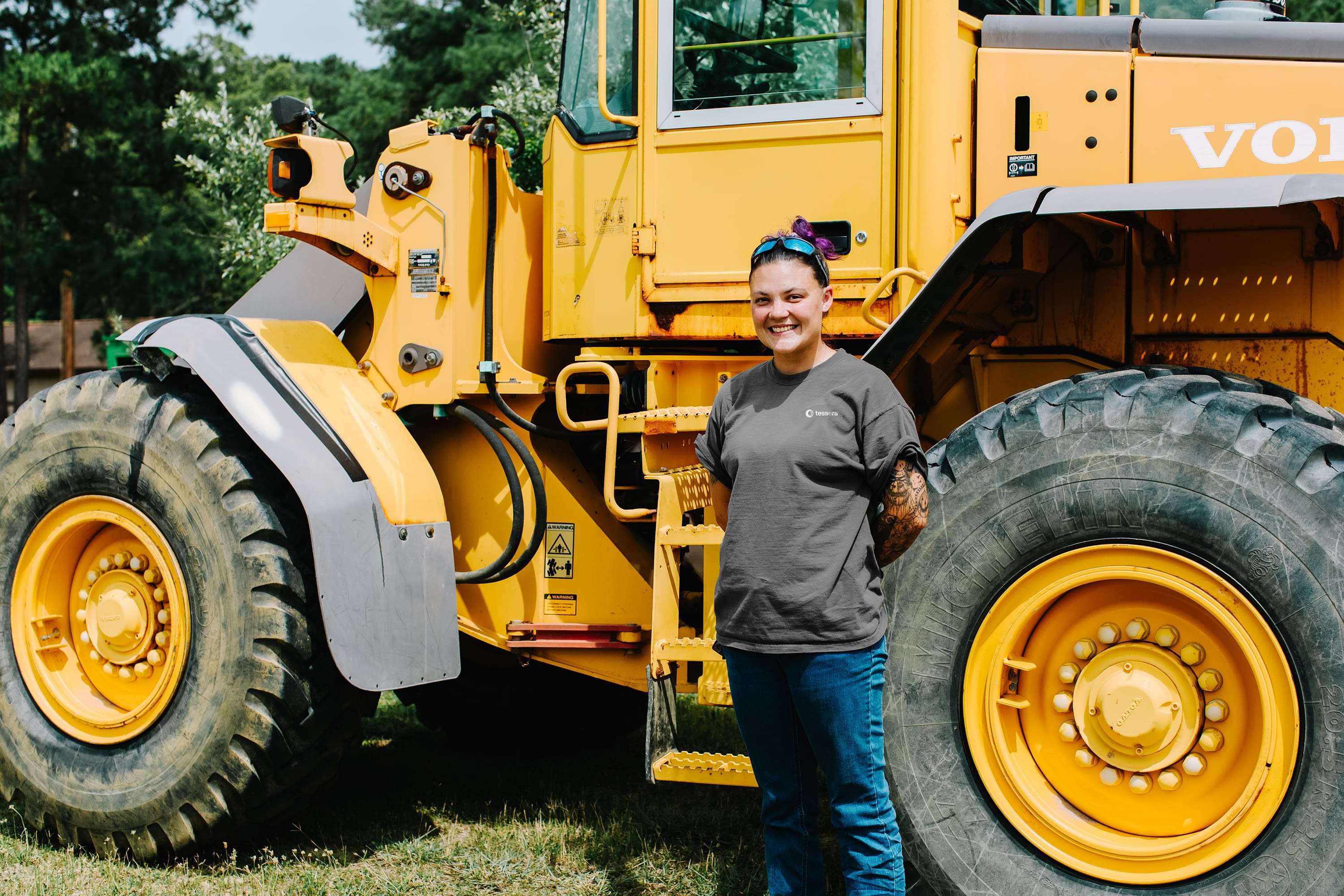 Tessera employee standing in front of large, yellow "construction" vehicle with large tires, similar to dump truck tires.